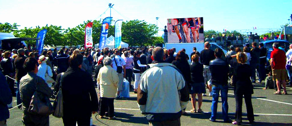 Installation d'un camion écran géant LED diffusant une course cycliste devant une grande foule