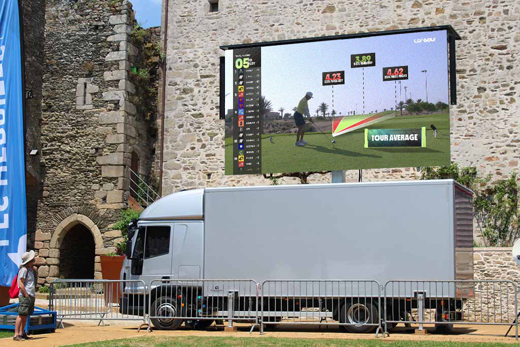 Camion régie avec écran géant LED plein jour diffusant une compétition de golf devant un vieux château en pierre